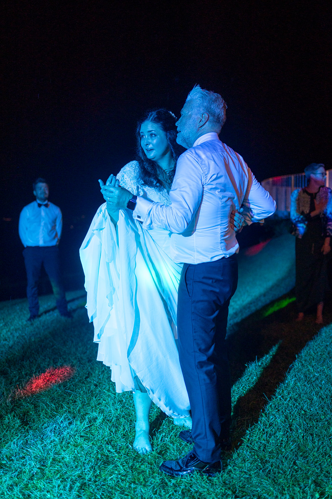 Bride and groom sharing intimate first dance on grass under blue lighting at outdoor evening wedding reception